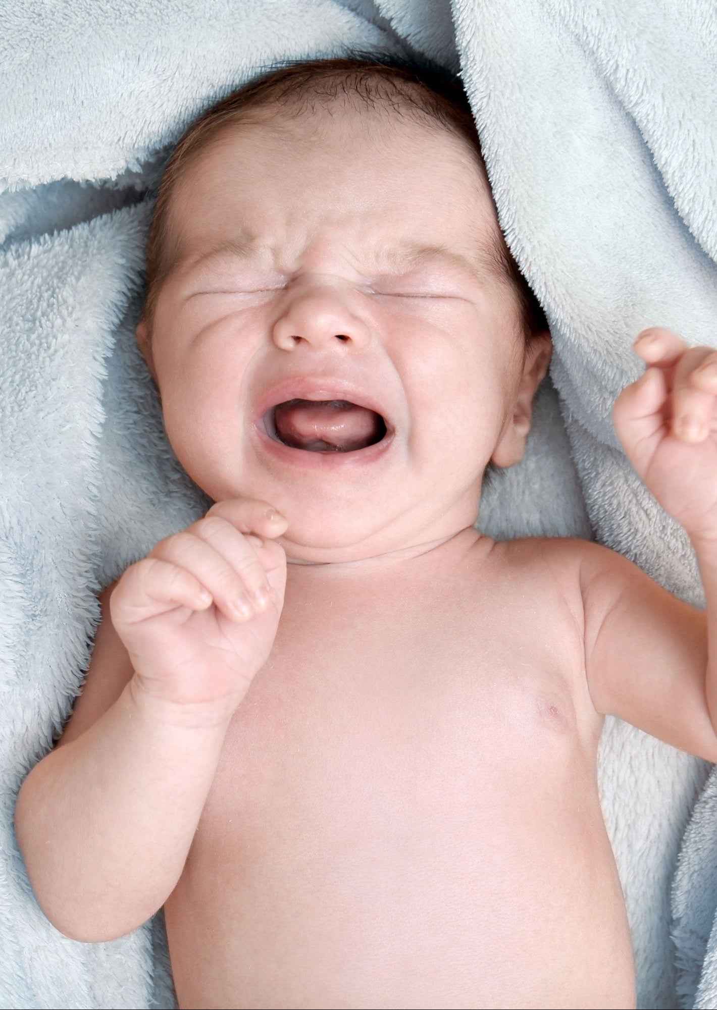 A newborn baby crying while lying on a soft blue blanket.