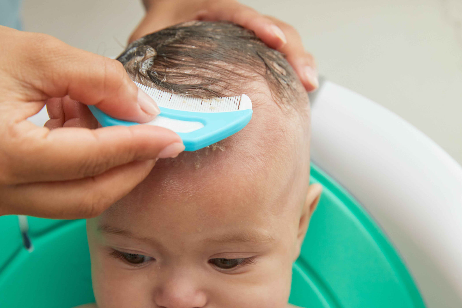 A parent gently combing a baby's scalp with the Flake Fixer comb at bath time.