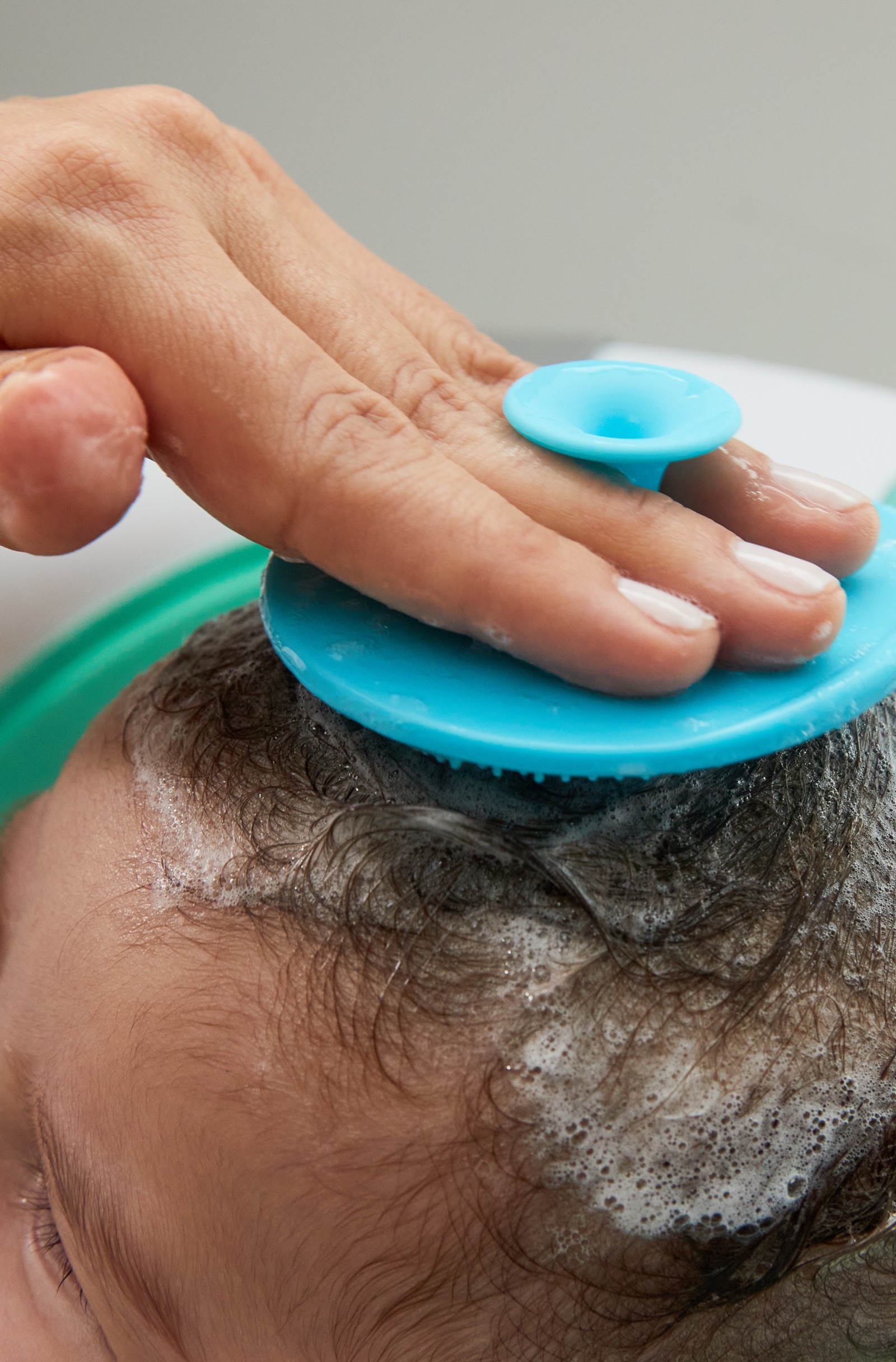 A parent brushing a baby's soapy scalp with the Skinsoother during a bath.