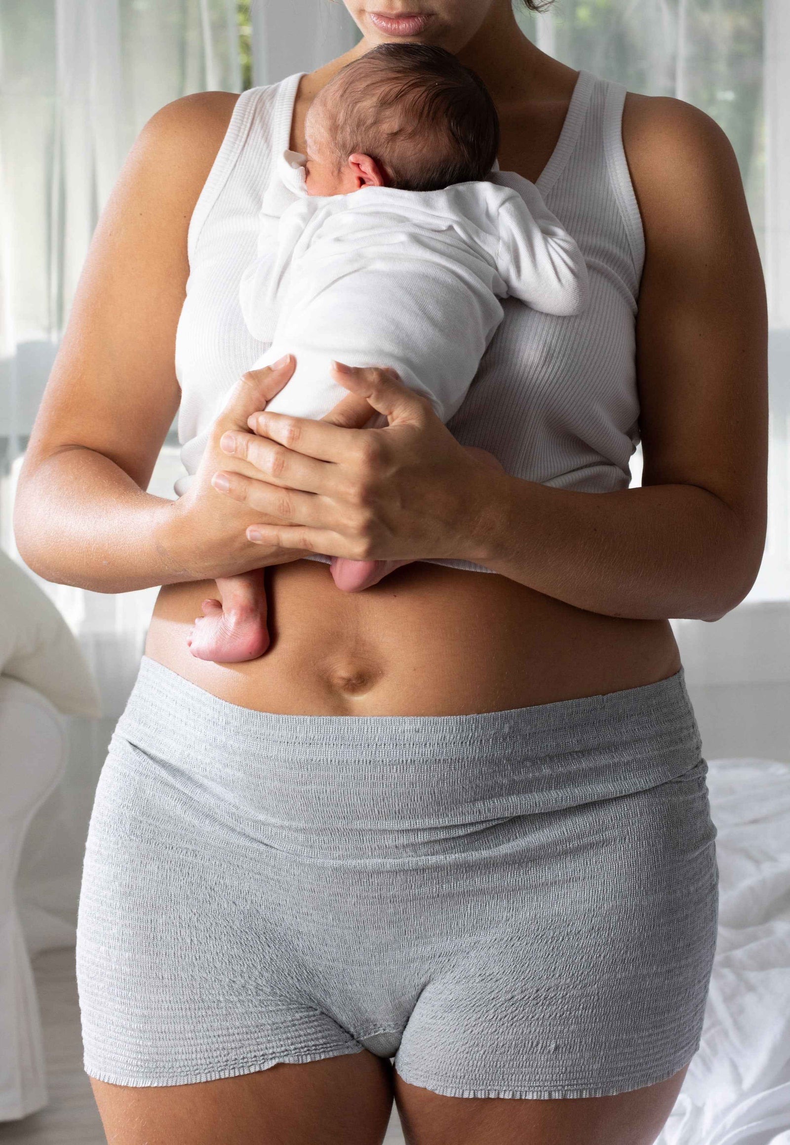 A new mum wearing Frida Mom disposable boyshort underwear while holding her newborn against her chest.