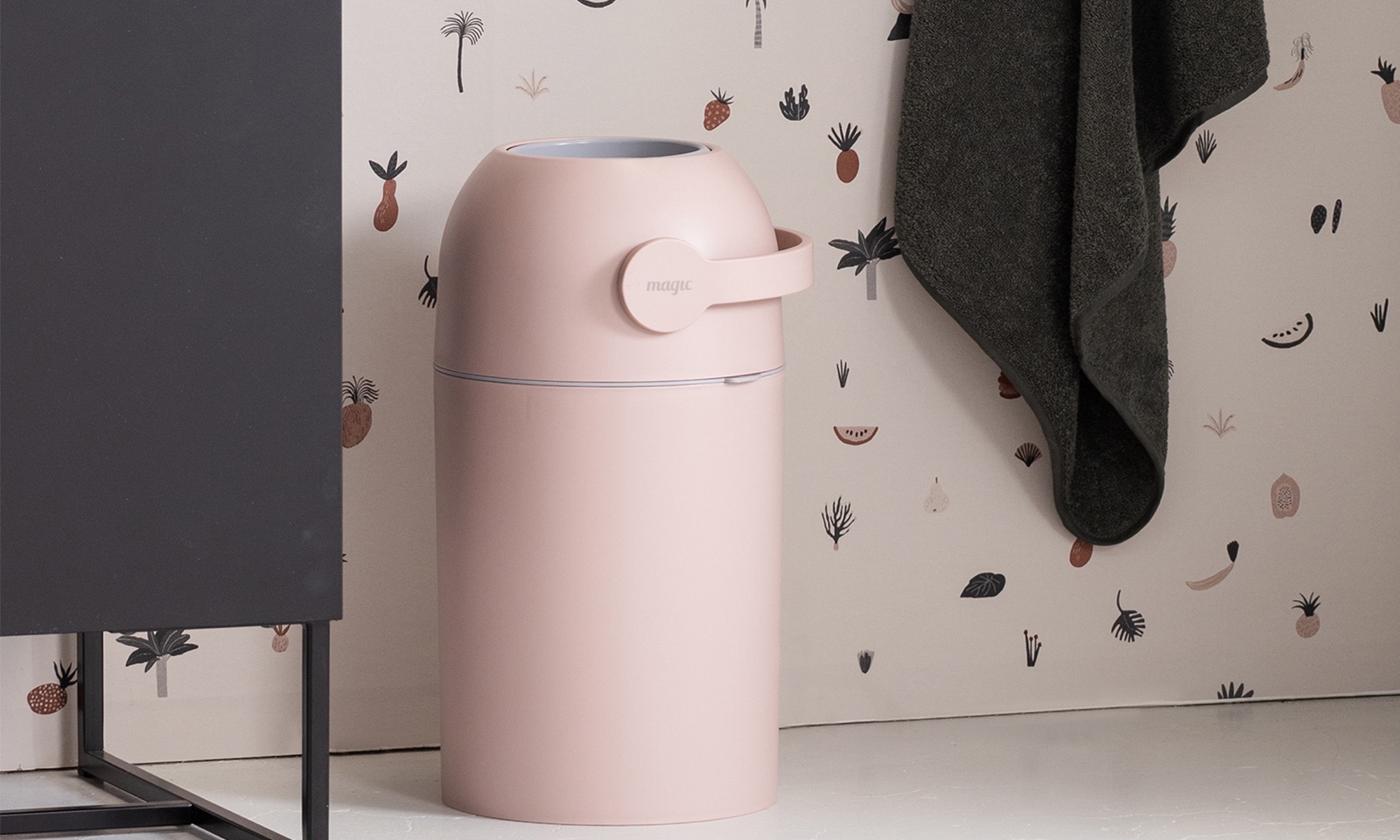 A pink Magic Majestic nappy bin in a bathroom beside a hanging towel