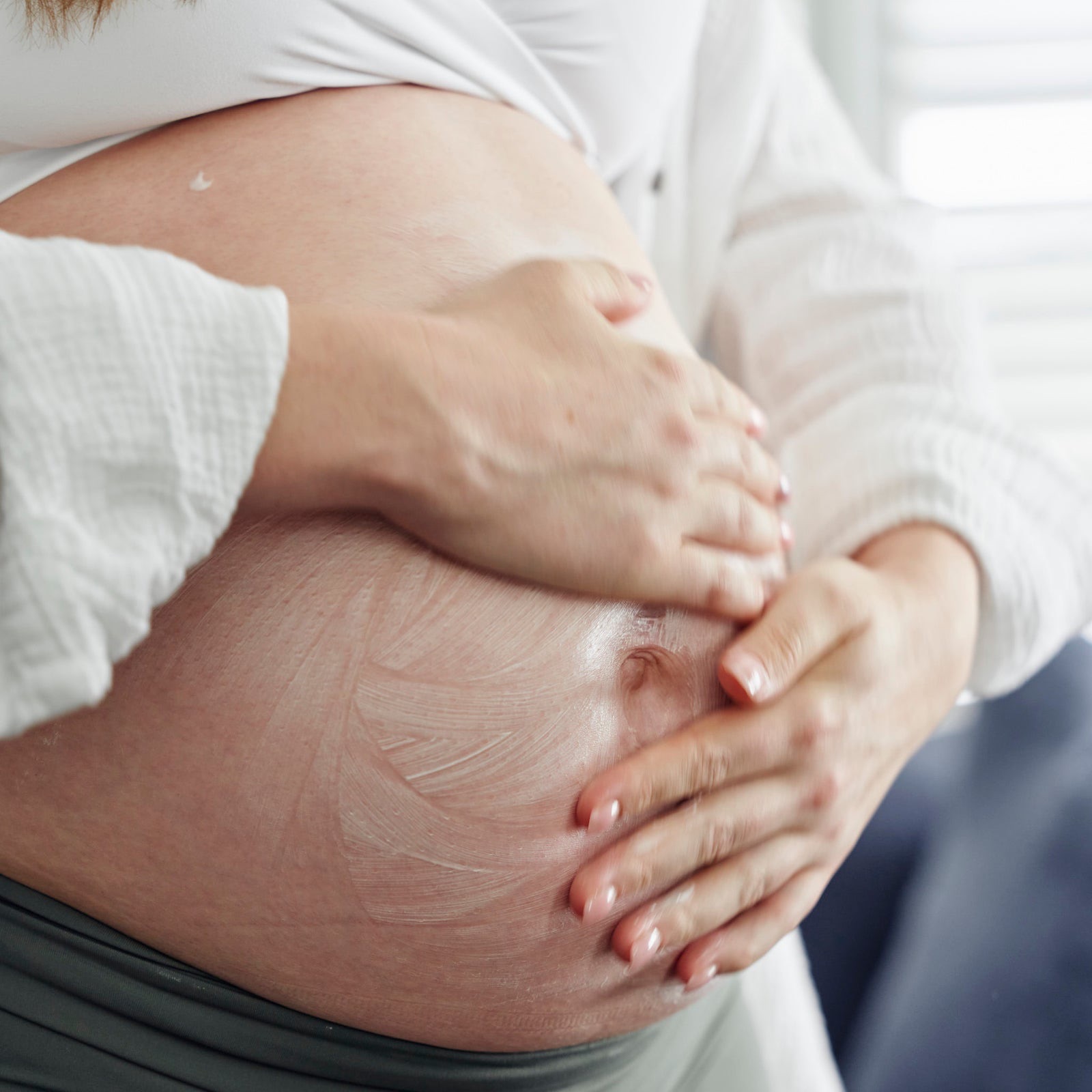 A pregnant woman massaging moisturiser into her bump.
