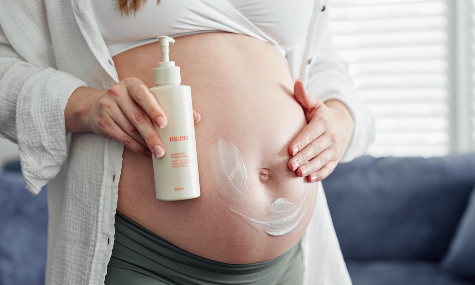 A pregnant woman holding a Mamave pump bottle with cream applied to her bump.