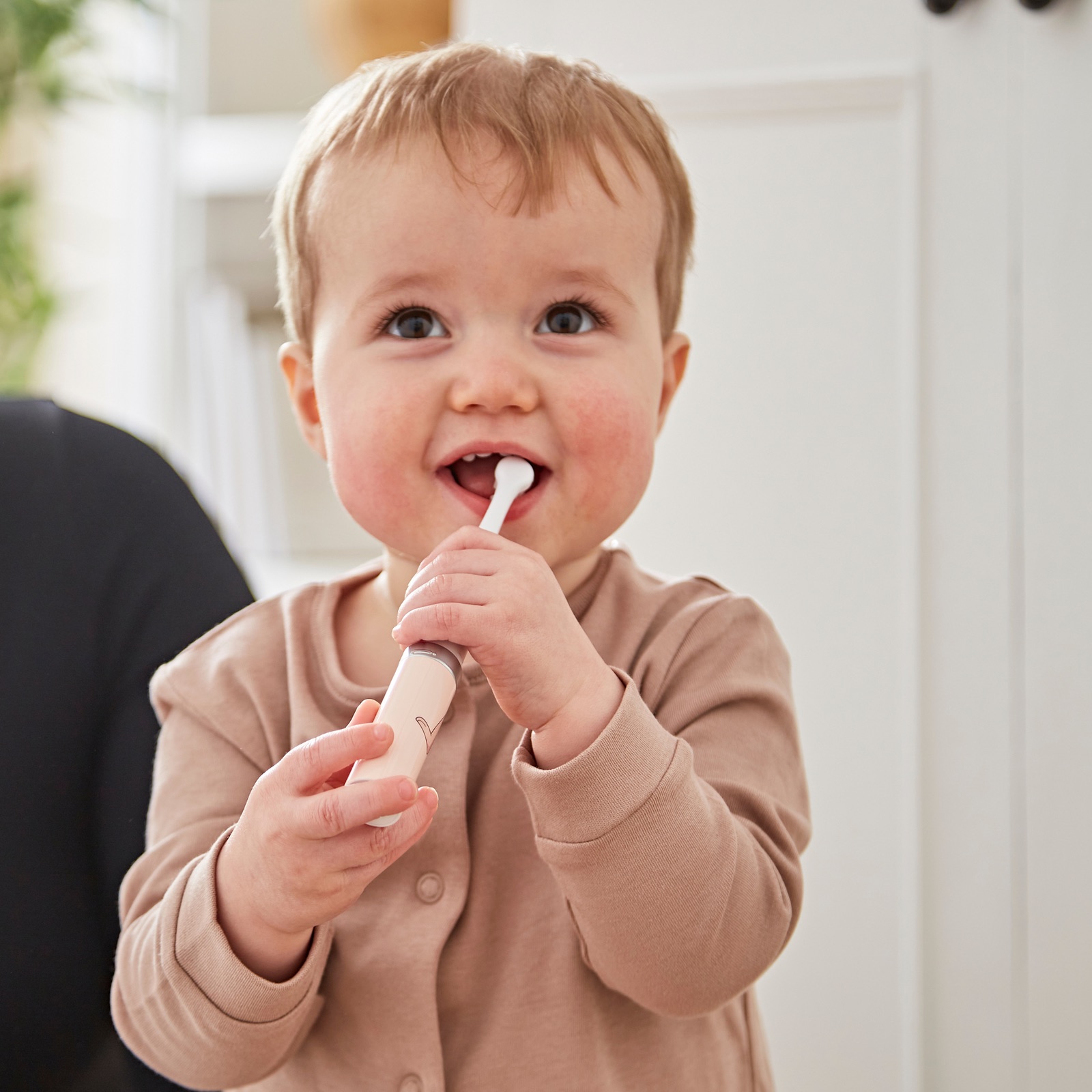 Smiling toddler brushing with a Dusty Pink Matchstick Monkey Baby Sonic Toothbrush.