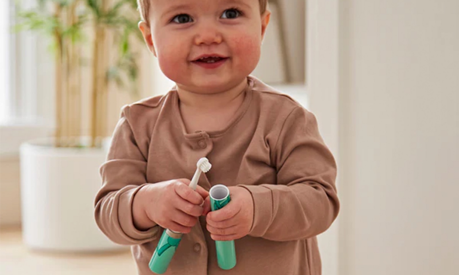 Smiling toddler standing in a living room holding a baby toothbrush.