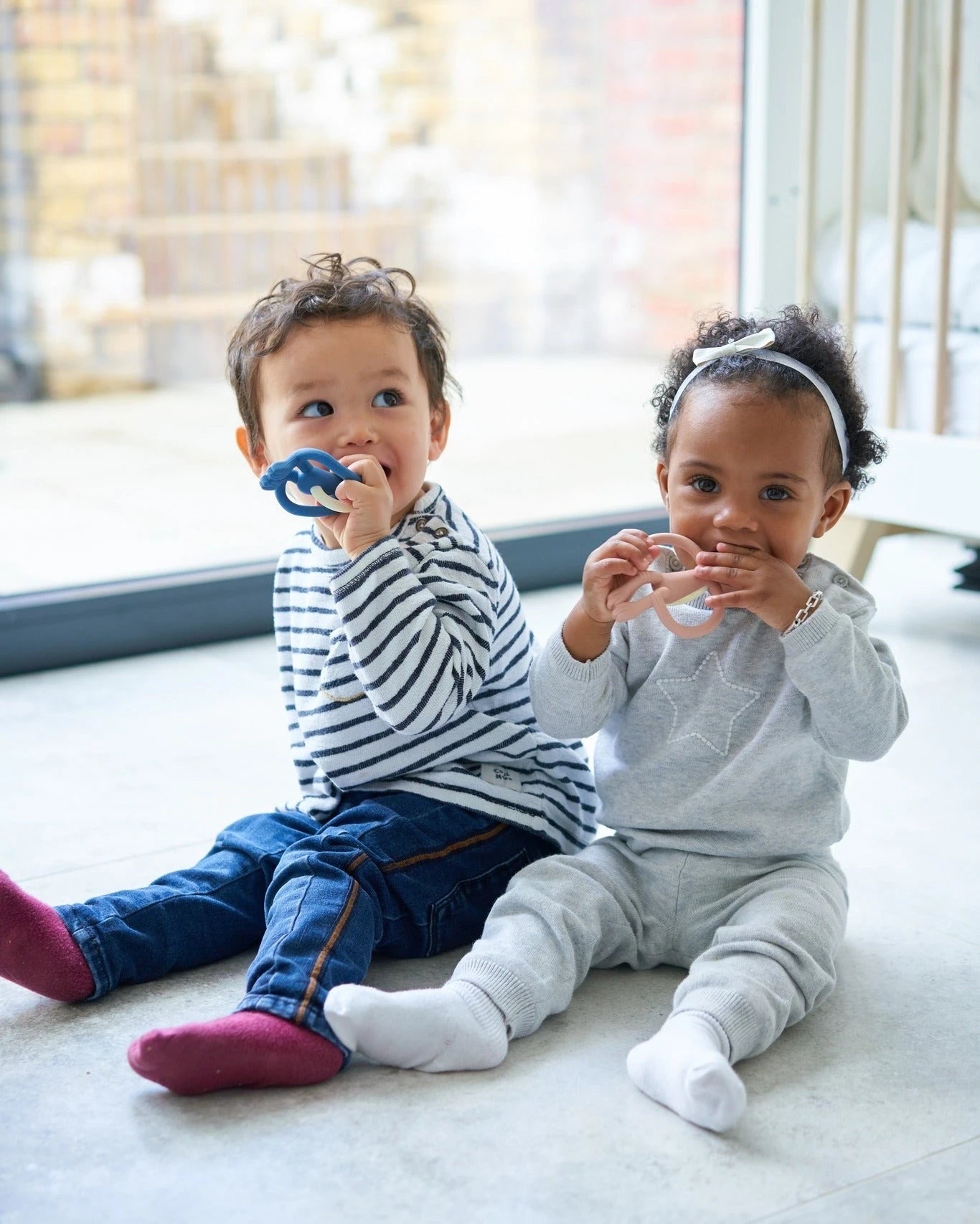 Two toddlers sitting on the floor, each chewing their own Matchstick Monkey teether.