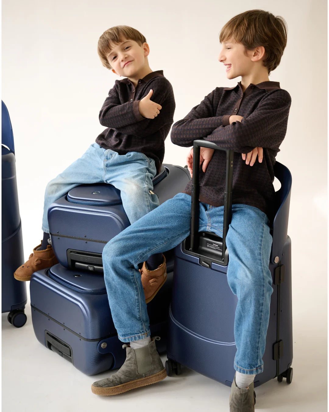 Two boys sitting on navy MiaMily Plus suitcases