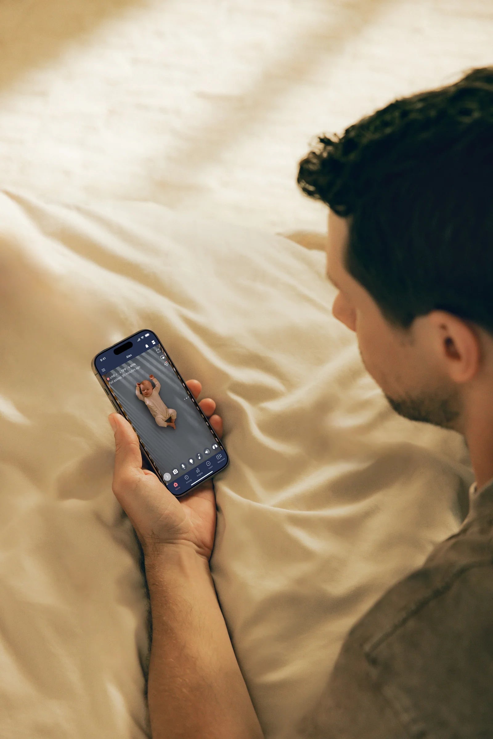 Father lying in bed checking the Nanit app live view of his baby on his phone.