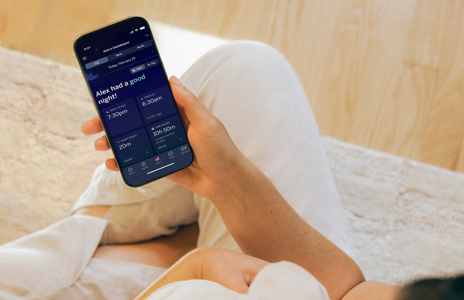 Parent holding a phone showing a Nanit nightly sleep summary with bedtime, wake time and time asleep.