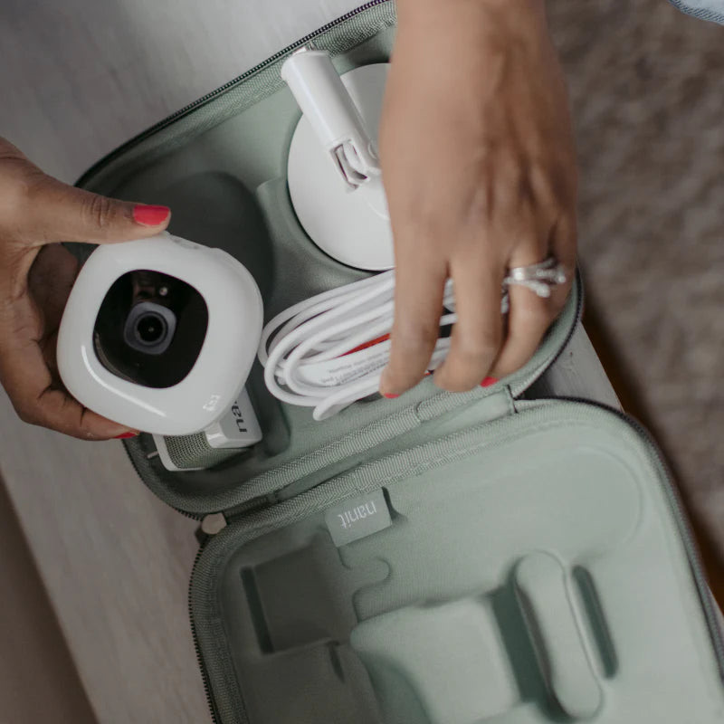 Hands packing a Nanit camera, stand and cable into the green Nanit Travel Case.