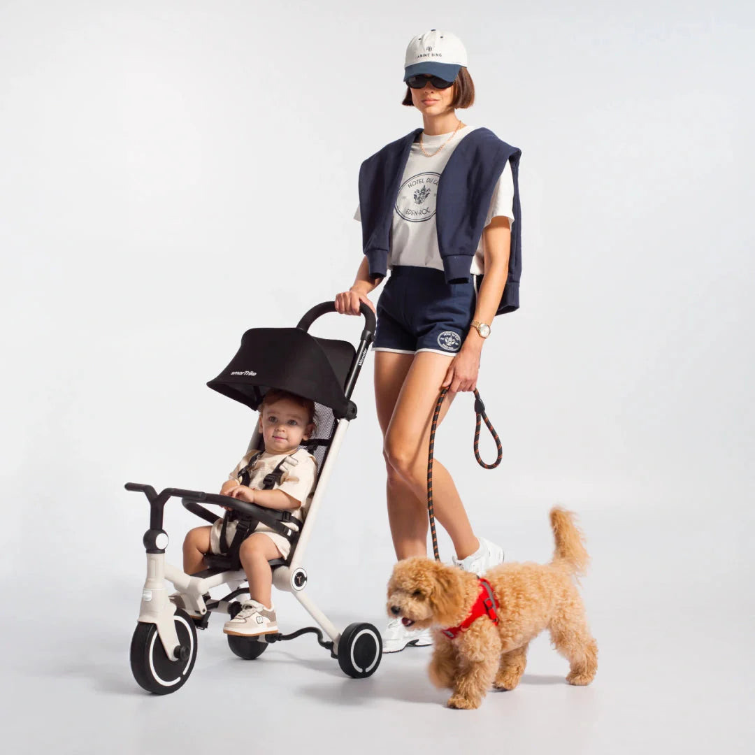 A parent walking a small dog pushes a toddler in a smarTrike Wonder in Moonlight, with a white frame and black canopy.