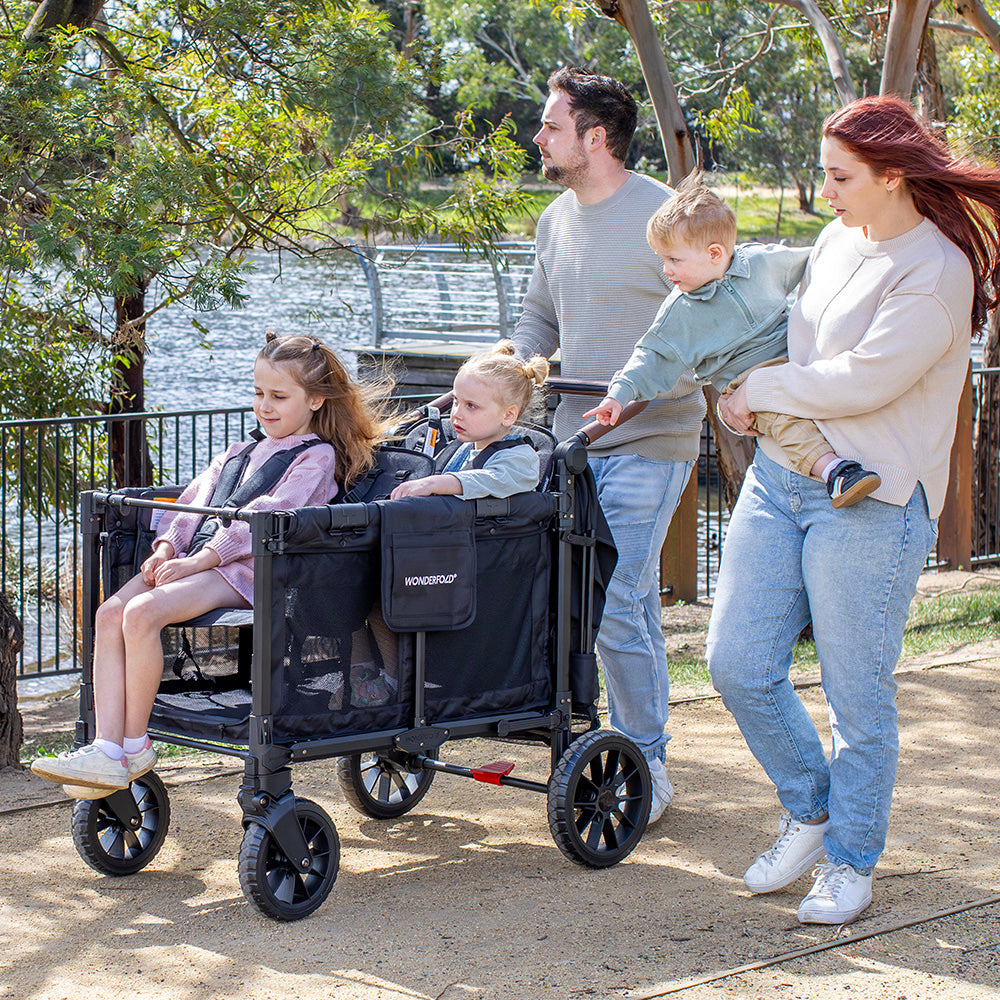 Family walking beside a WonderFold W4 Luxe Pro with two children seated inside and a toddler carried