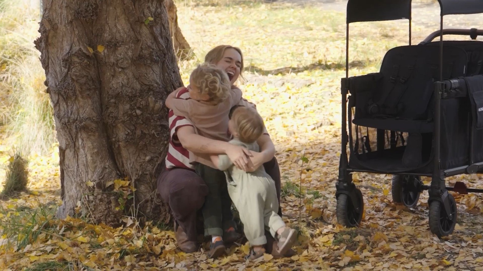 Mother hugging two young children under a tree beside a WonderFold stroller wagon