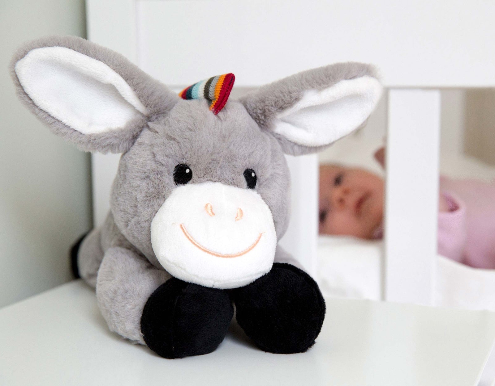 Don the Donkey white noise soft toy on a shelf beside a cot with a baby inside.