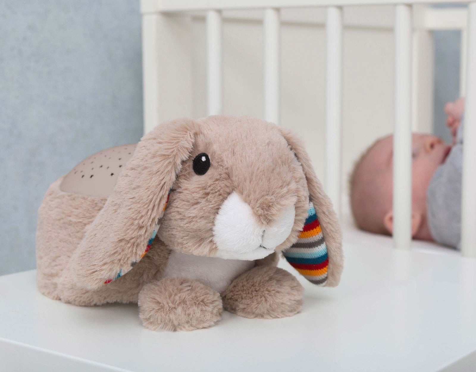 Ruby the Rabbit star projector on a shelf beside a cot with a baby inside.
