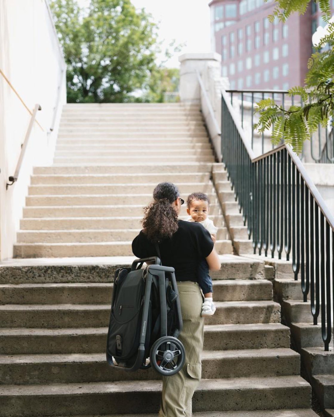 A parent carrying a folded UPPAbaby pram up steps