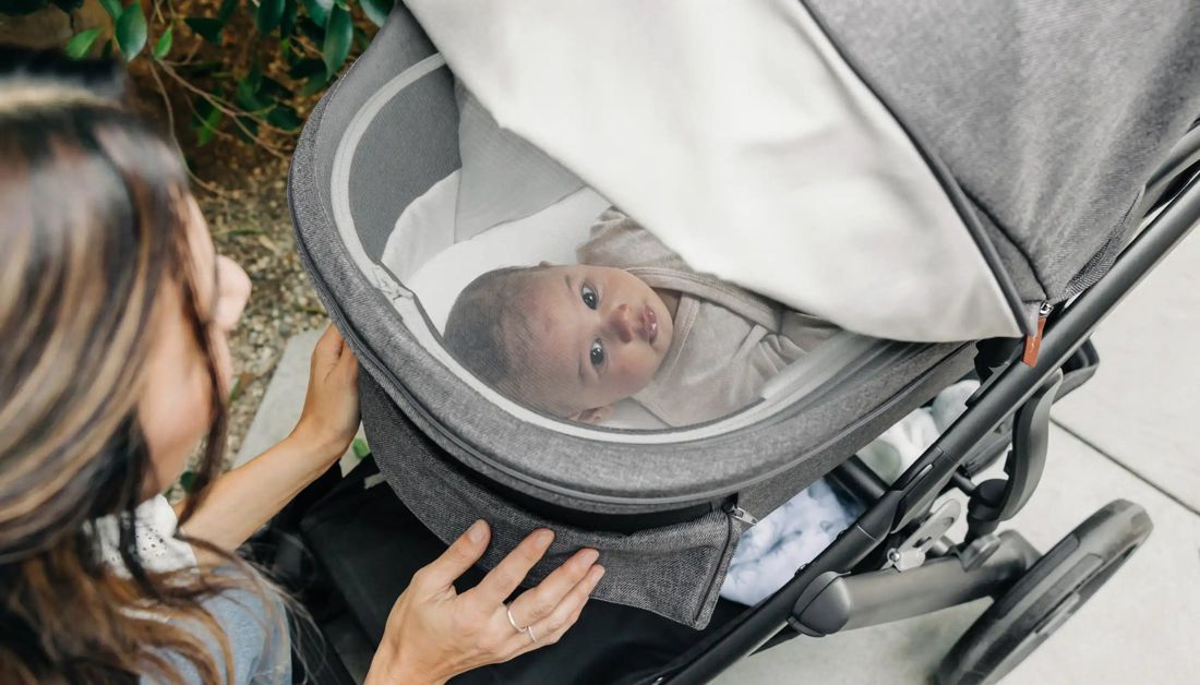 Overhead close-up of a mum's hands on a grey bassinet as a newborn looks up from inside