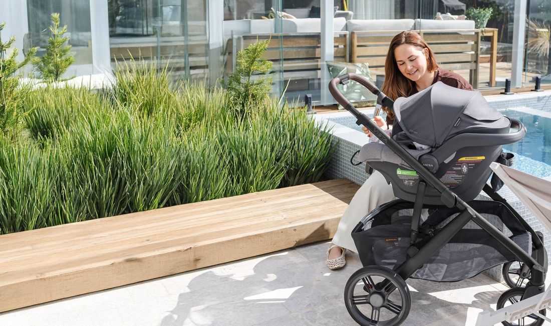 A mum sits on a sunny terrace beside a baby in a Mesa capsule clicked onto a Vista V3.