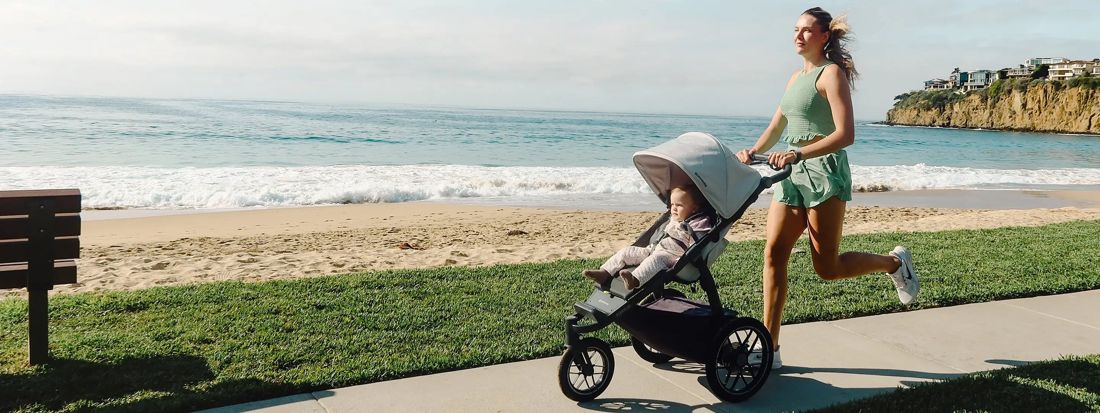 A mum runs pushing a Ridge jogger with a toddler along a beachfront path.