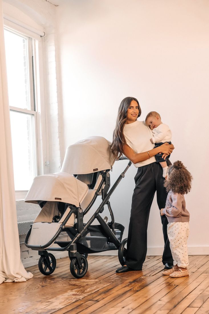 A mum holding a baby, with a toddler beside her, stands next to a sand-coloured Vista V3 fitted with a RumbleSeat.