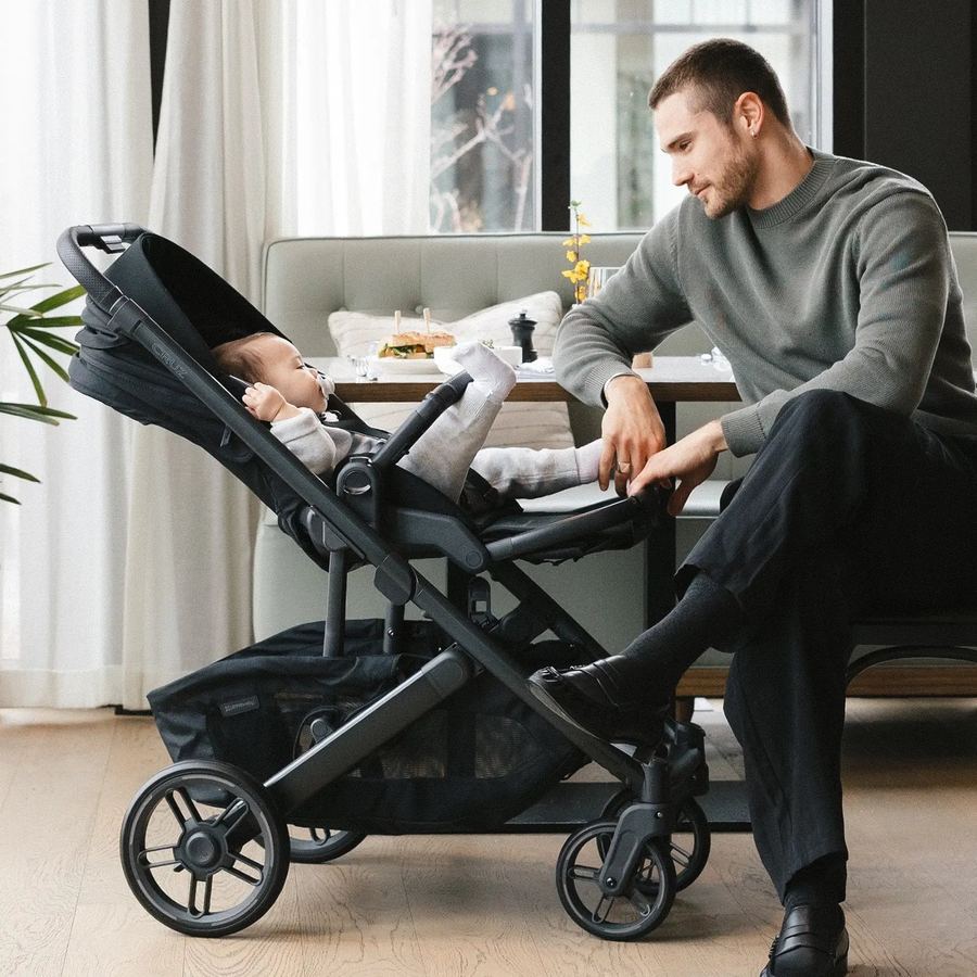 Dad sits in a cafe booth leaning towards a baby reclining in a black Cruz V3