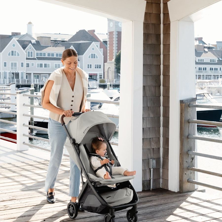 Smiling mum pushes a light grey Minu V3 with a baby on a sunny marina boardwalk