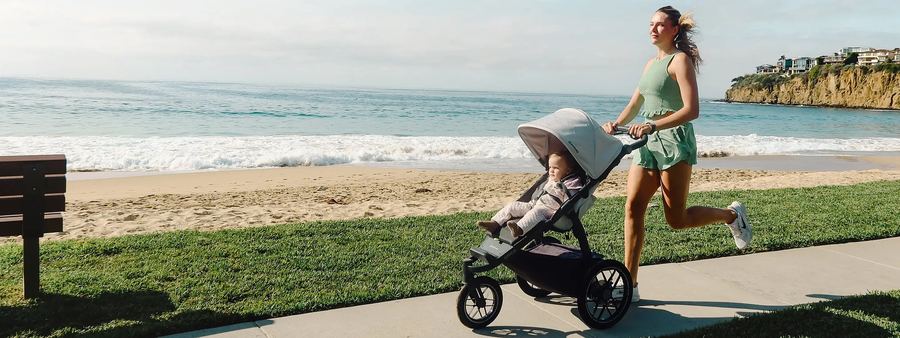 Mum runs pushing a Ridge jogger with a toddler along a grassy beachfront path beside the ocean