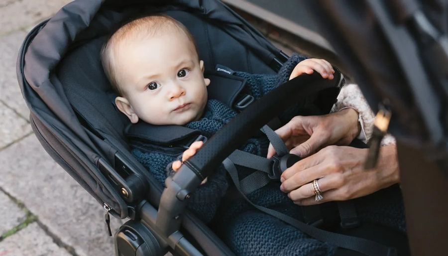 Close-up of a parent's hands buckling the five-point harness on a baby seated in a charcoal RumbleSeat