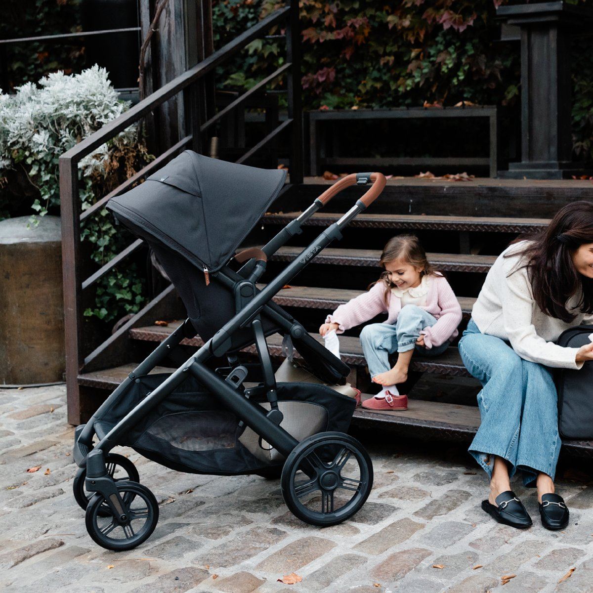 Vista V3 parked on cobblestones beside outdoor steps where a young girl puts on her shoes next to her mum